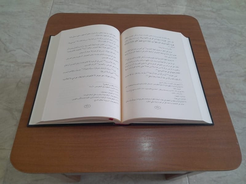 Livre islamique ouvert et posé sur un petit bureau en bois.